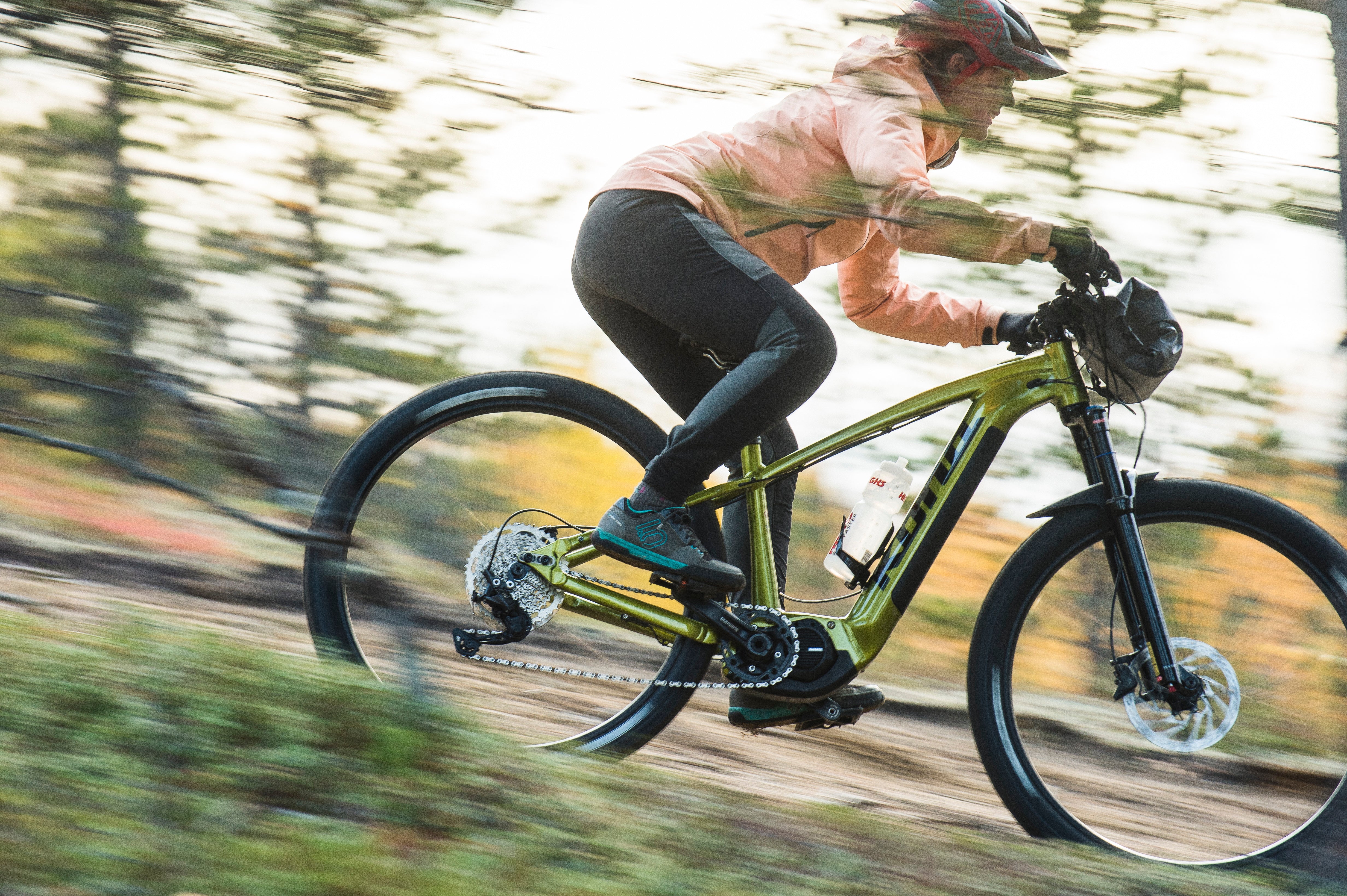 Person riding a green bicycle on a trail with trees in the background