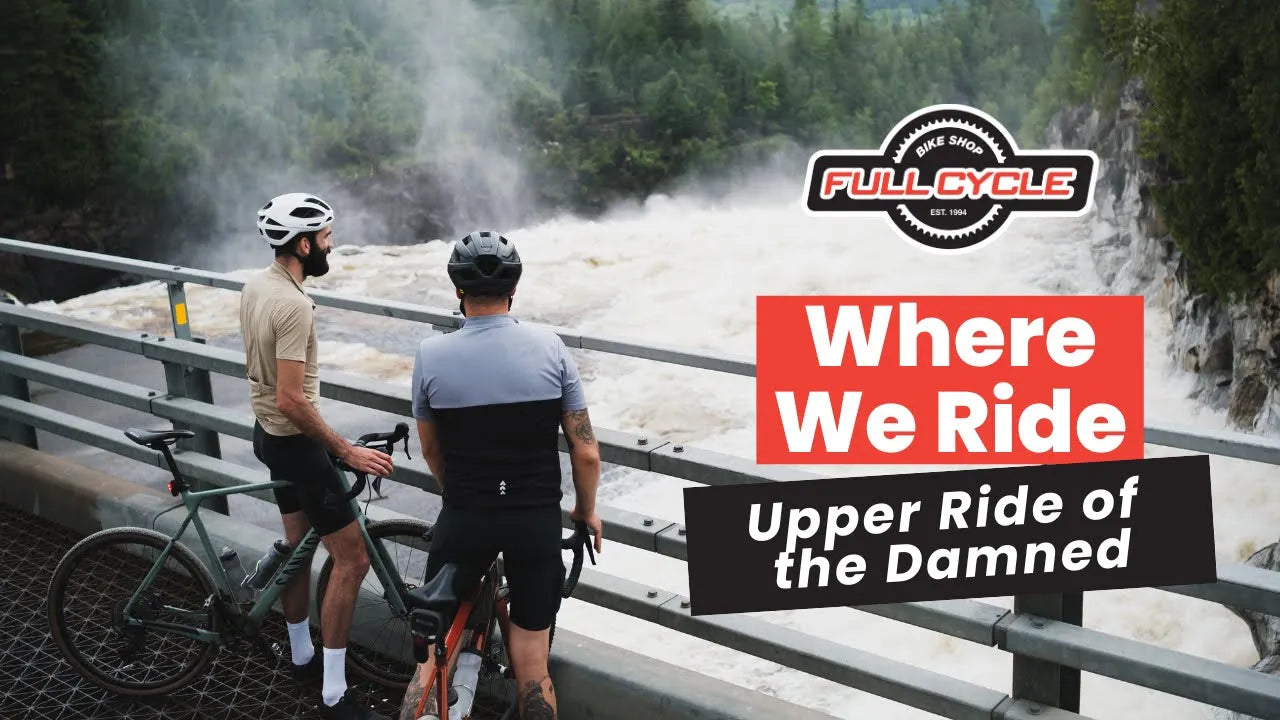 Two cyclists standing next to a river with a sign that reads 'Where We Ride' and 'Full Cycle' branding.